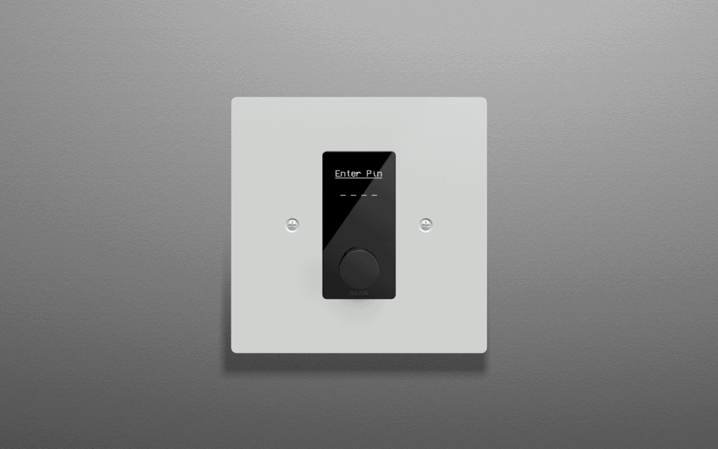 Xilica Designer IP-Based Wall Control featuring a recessed rotary encoder and configurable OLED display, designed with a white coated aluminium faceplate for EU/UK wall-box installations.